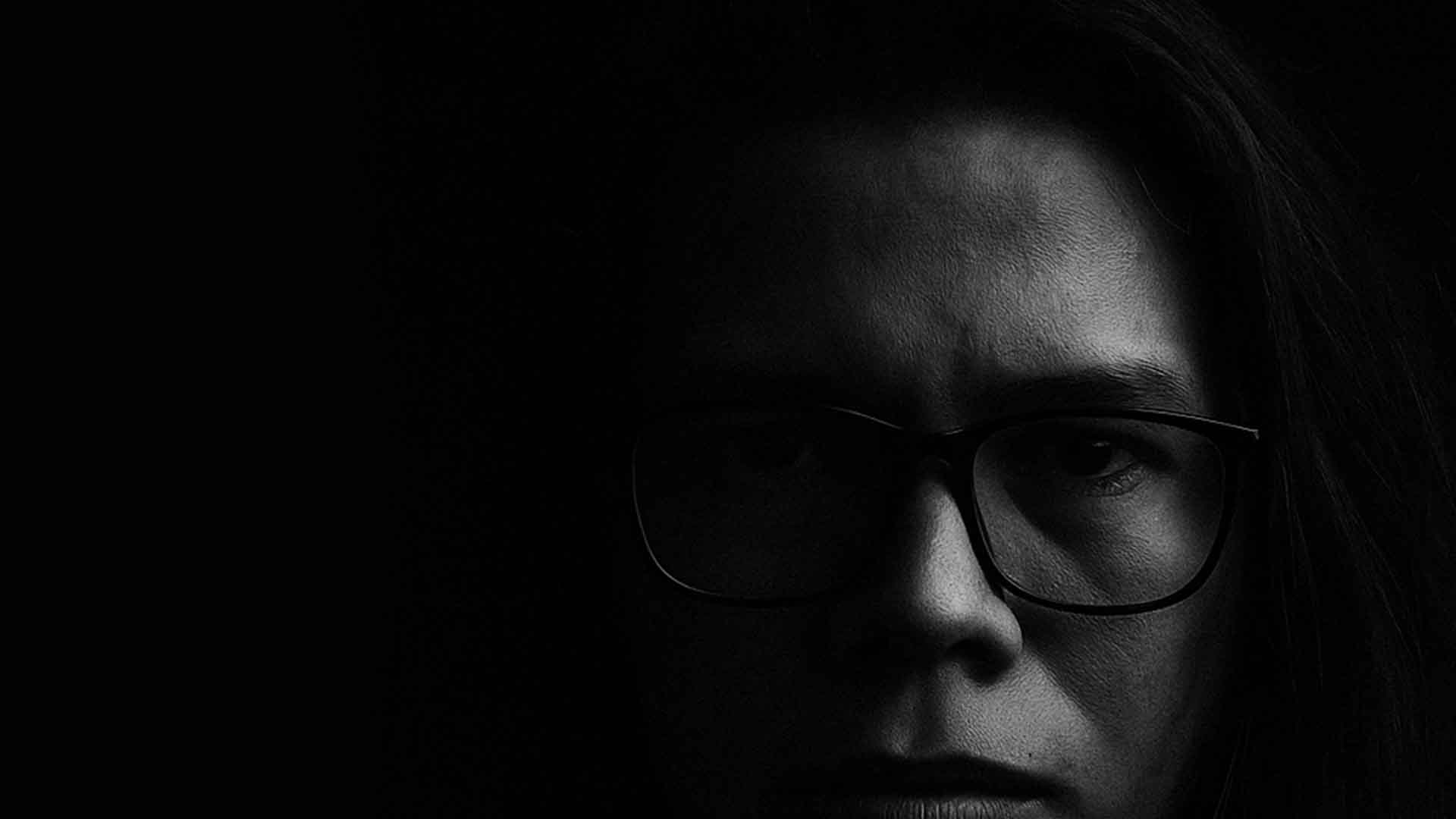 Retrato en blanco y negro de Carlos Castillo, con gafas, en primer plano sobre fondo oscuro